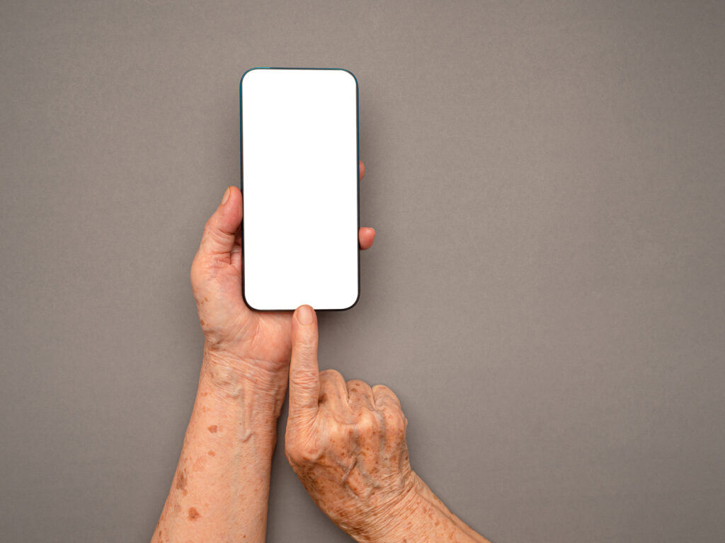 An elderly person's hands holding a smartphone with a blank screen. This image could represent the growing use of technology among older adults, including apps designed to support their needs.