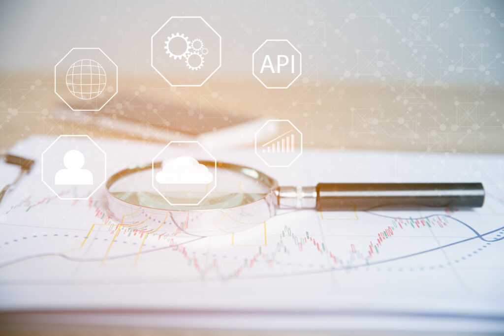 This image depicts a magnifying glass placed over a chart or graph, with various icons representing different aspects of software development, such as a person, a cloud, gears, a globe, and a line graph. The word "API" is prominently displayed, suggesting the image is related to Application Programming Interfaces (APIs) and their role in software development.