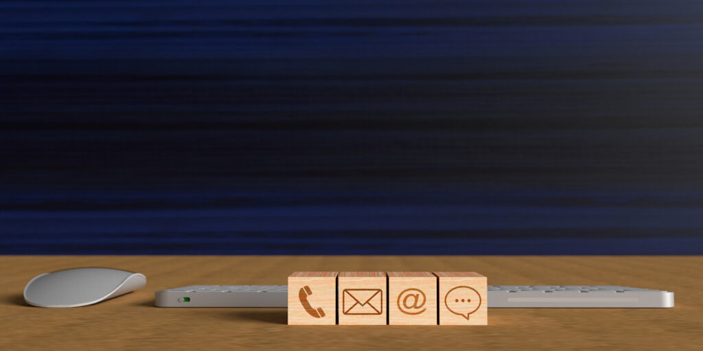 Wooden blocks with phone, email, at, and chat symbols on a desk with a keyboard and mouse