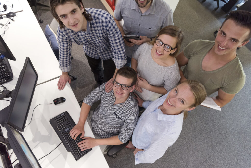 A team collaborates around a computer workstation, emphasizing backend software development as one person types code while others provide input. The scene highlights teamwork and technical focus on backend processes.