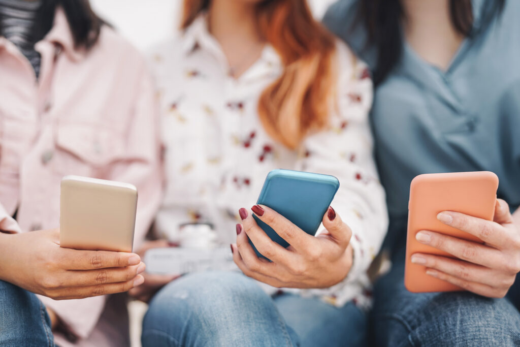 Three individuals engaging with their smartphones, symbolizing the role of AI in digital marketing as it analyzes consumer behavior and personalizes marketing strategies through mobile devices.