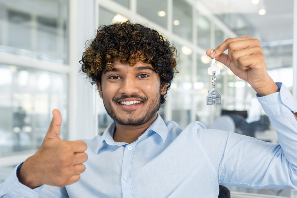 A happy real estate agent gives a thumbs up while holding house keys, representing the confidence and precision achieved through accurate Automated Valuation Models (AVM) in property transactions.