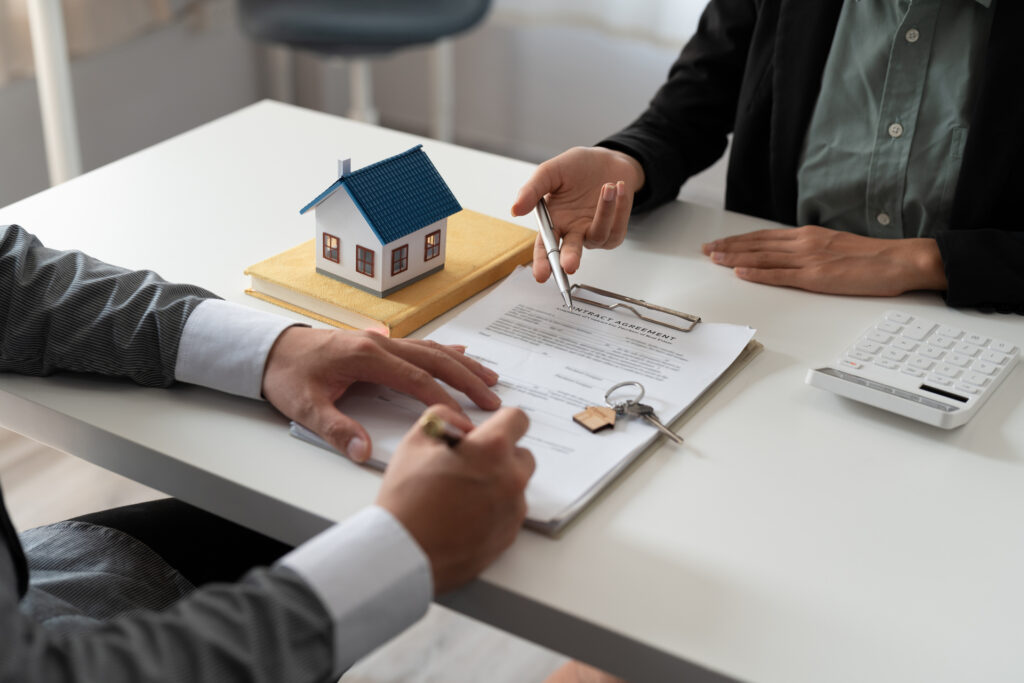 A miniature house model placed on top of a house blueprint with a key nearby. 