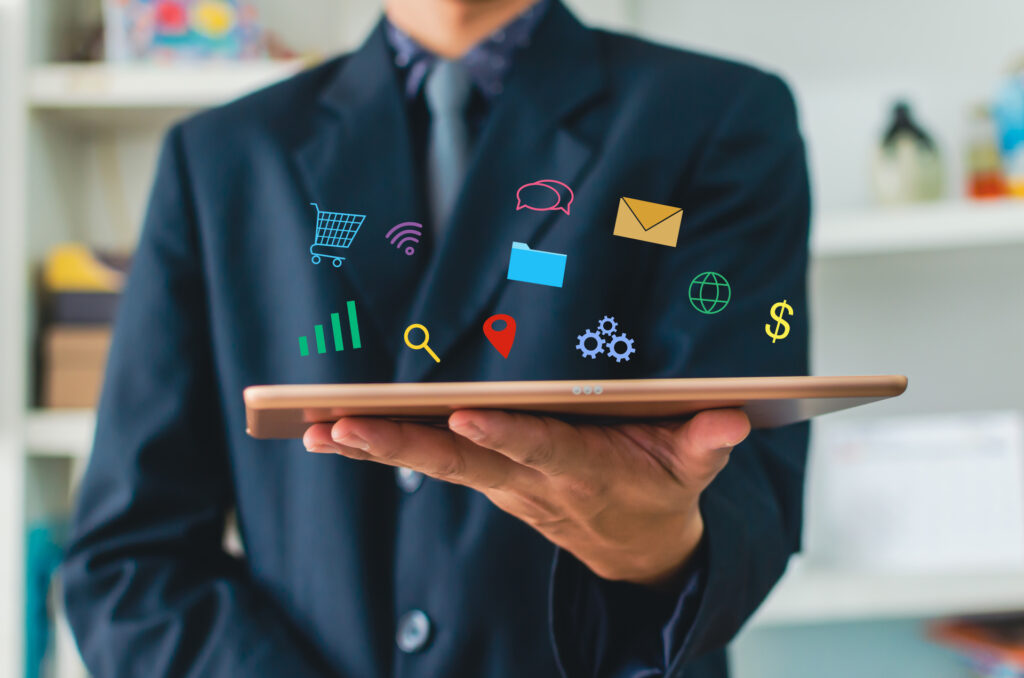 a person is holding a tablet with various digital icons floating above it, which represent different aspects of marketing, such as shopping carts, communication tools, search icons, location markers, and financial symbols