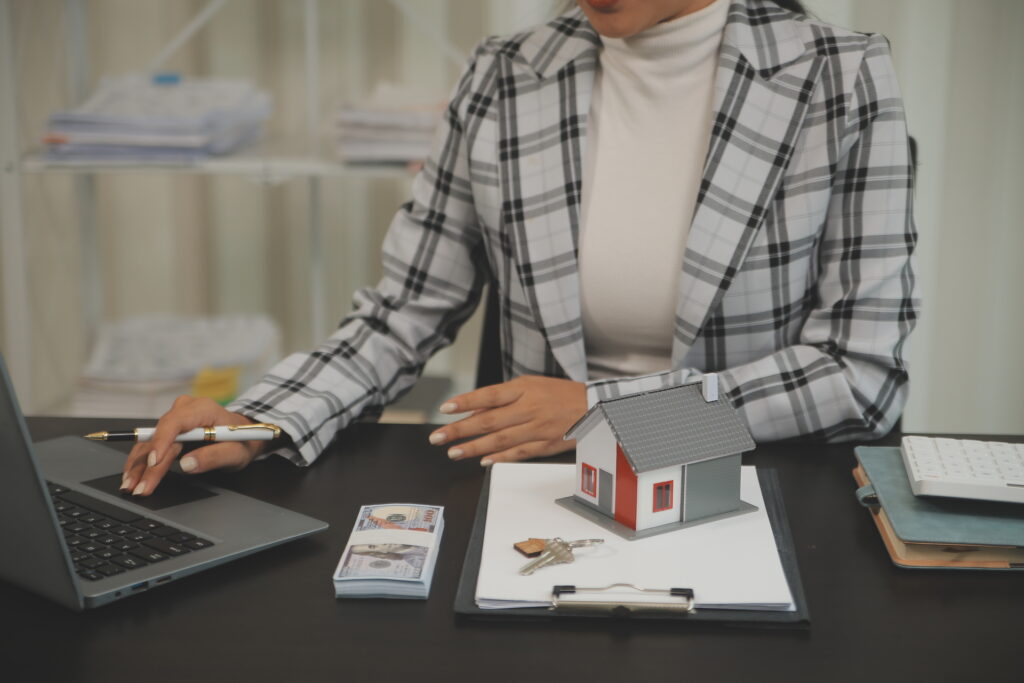 A real estate agent using CRM software to manage commercial property transactions, with a model house and financial documents on the desk.