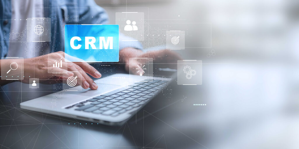 A person's hands on a laptop keyboard, with a blue box labeled 'CRM' and related icons hovering above.