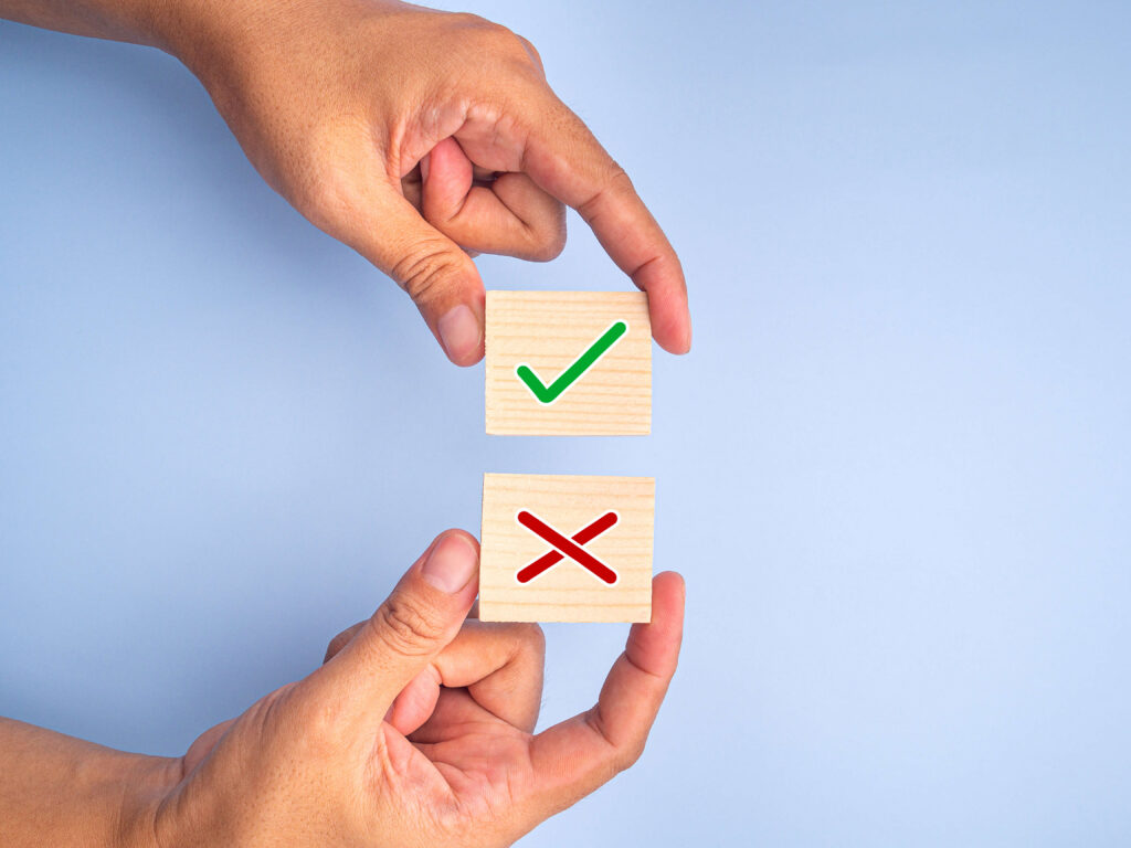 A pair of hands holding up two wooden squares. One square has a green checkmark, and the other has a red X. This image can represent the concept of making a choice or decision