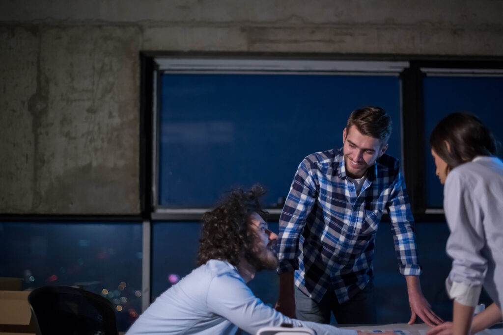 Image shows a group of people in a collaborative setting, likely working late at night, discussing plans or strategies