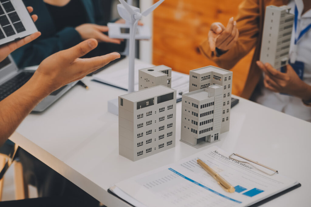 A group of people gathered around a table, discussing plans for a multifamily development. There are models of buildings, a wind turbine, and solar panels on the table.