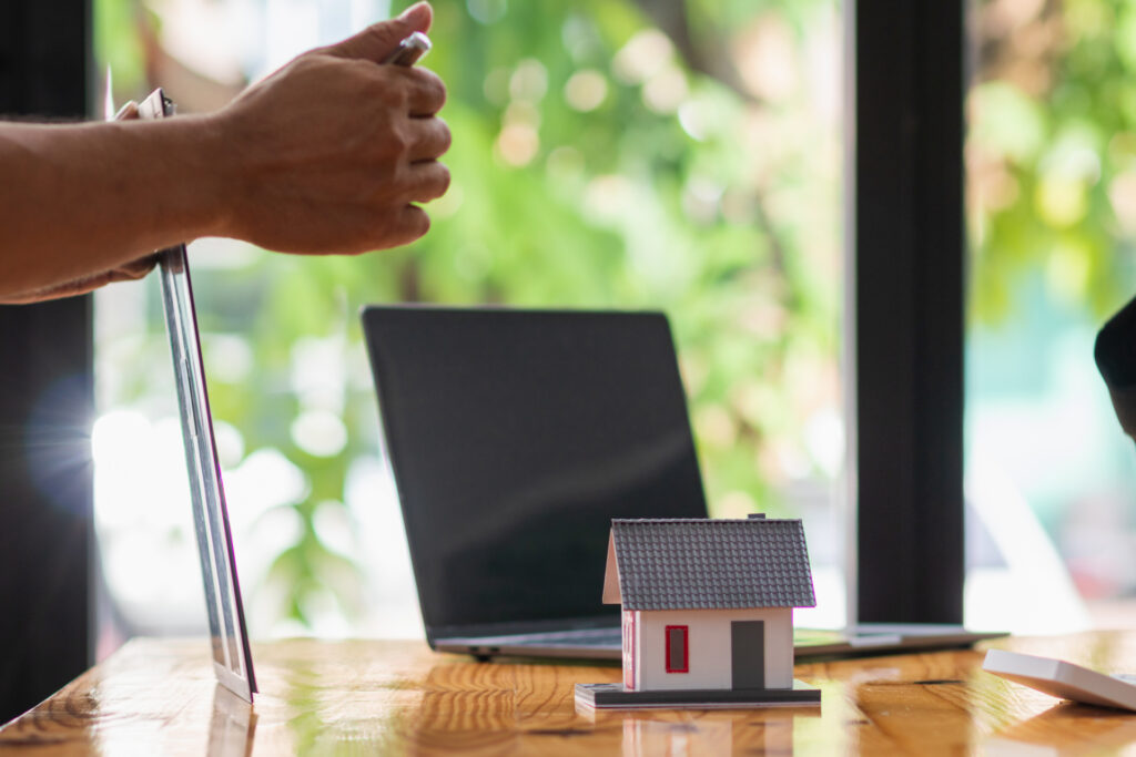 A real estate agent reviewing property details on a clipboard with a house model and laptop nearby