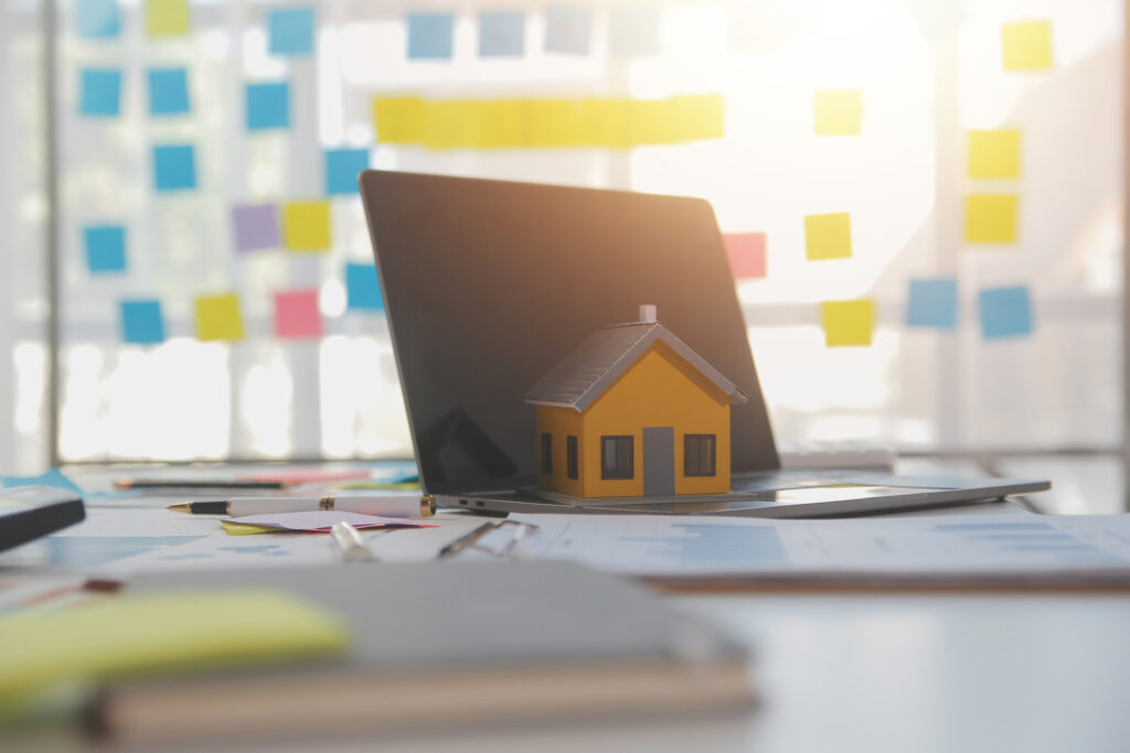 A laptop with a small house model on the screen, symbolizing real estate customer relationship management software.