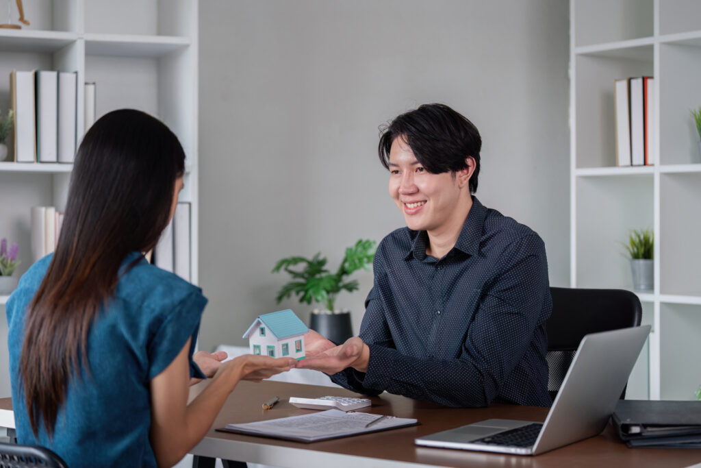 A real estate agent using CRM software to assist a client in purchasing a home, represented by the model house being exchanged.