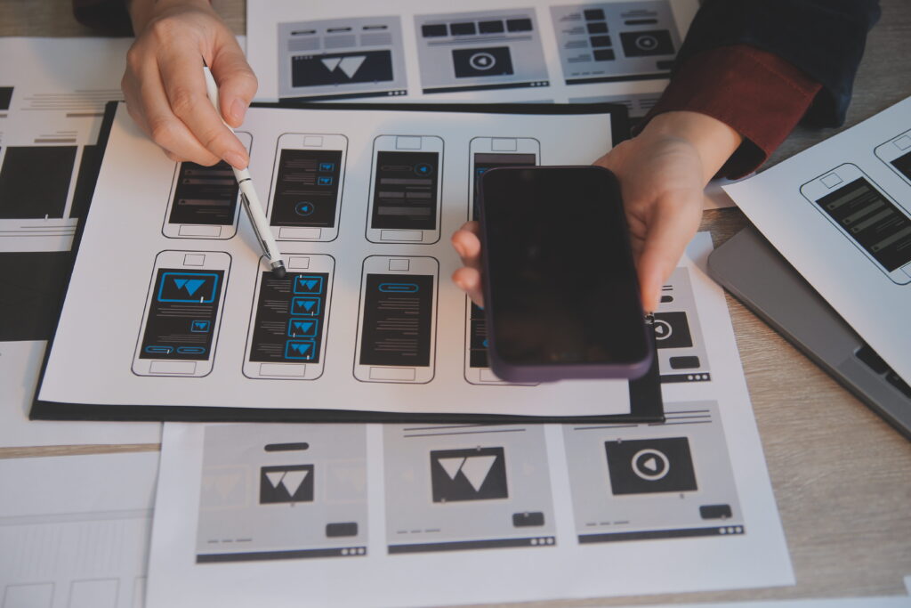 A team of designers reviewing wireframes and mockups for a new mobile app. They are using a smartphone to get a sense of the user experience.