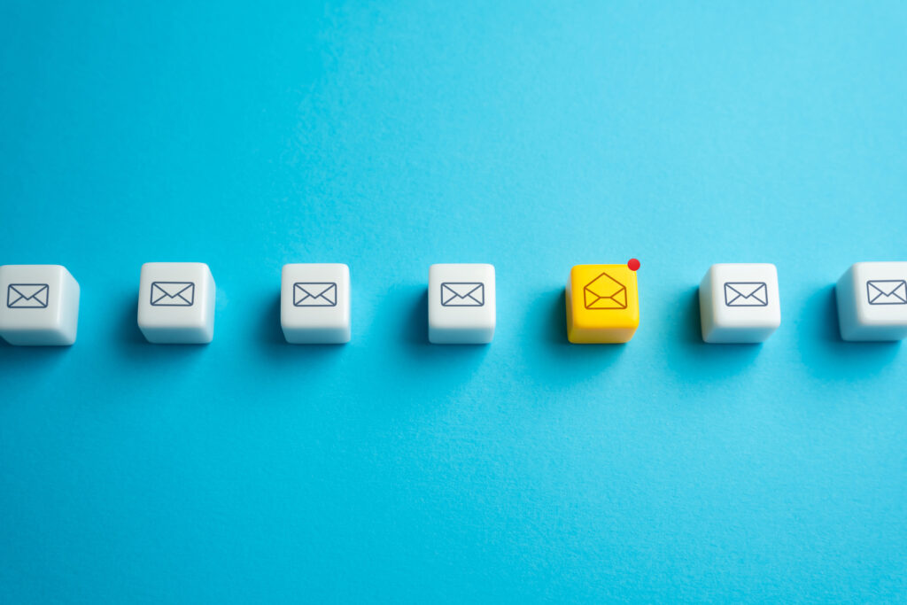 A line of white cubes with email icons, with one yellow cube standing out, emphasizing the importance of email marketing campaigns in attracting attention.