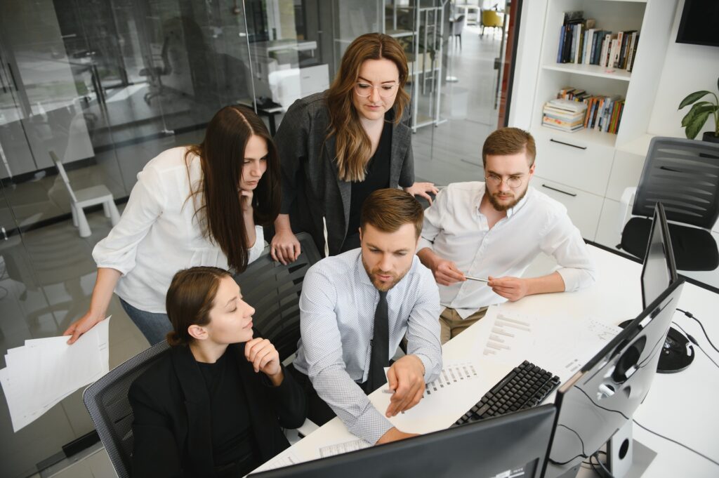 A group of professionals collaborates on marketing operations, analyzing data and discussing strategies around a desk with computers and documents.