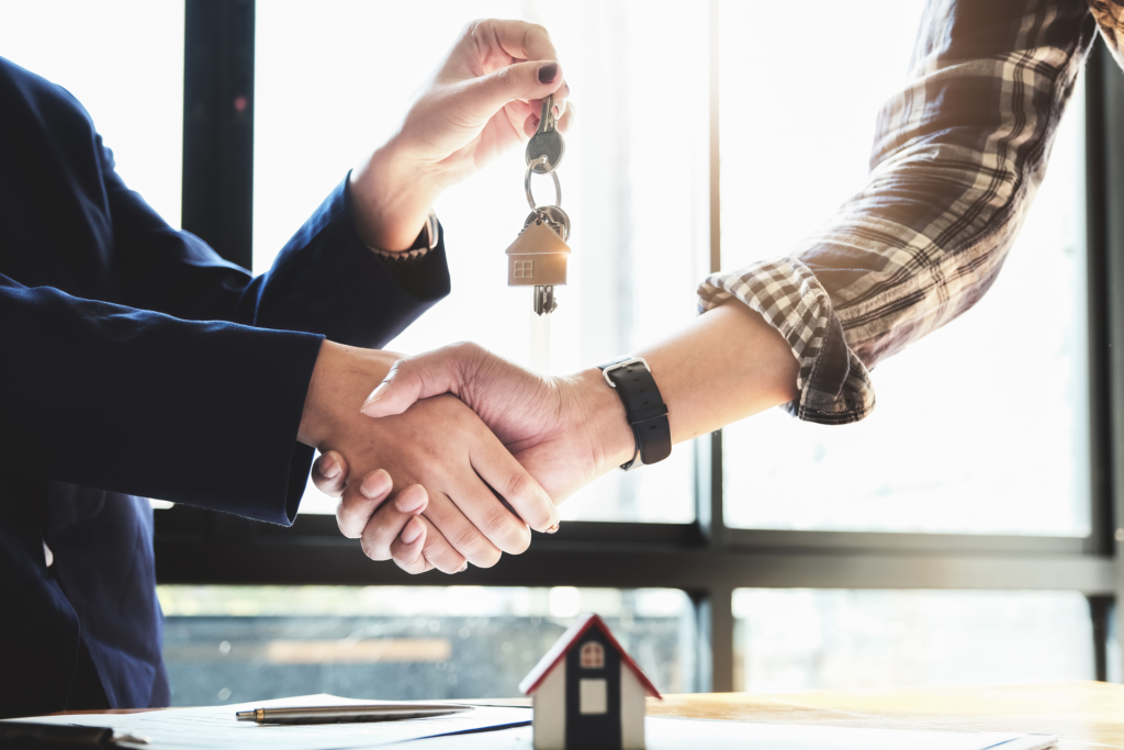 Real estate agent handing over keys to new homeowner and shaking hands, symbolizing property transaction success facilitated by real estate software.