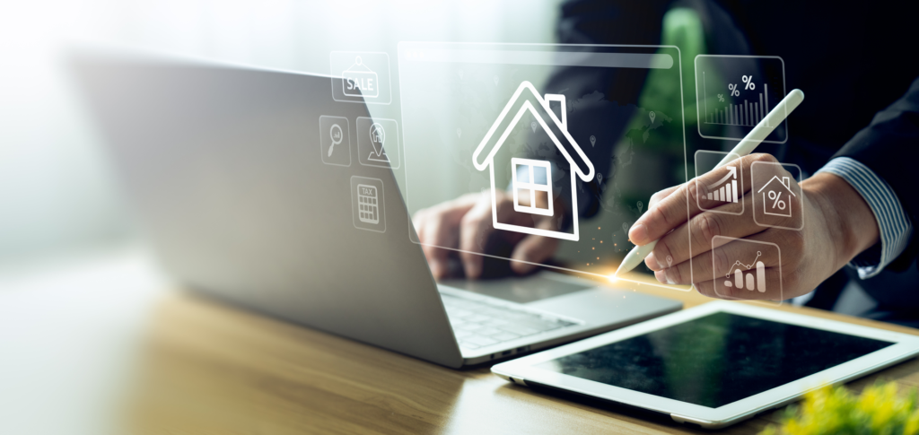 A person using real estate software on a laptop and tablet, with icons representing property sales, tax, and market analysis displayed on a transparent screen.