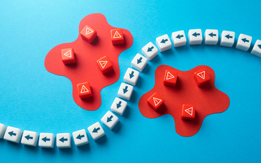 A conceptual representation of risk assessment with red cubes marked with warning symbols, surrounded by white cubes with arrows, indicating potential hazards and directions.