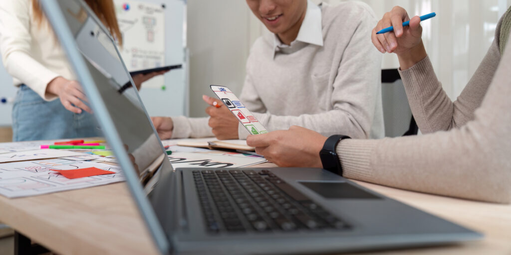 two people collaborating on a project, likely involving design or software development, as indicated by the laptop, charts, and markers visible in the image.