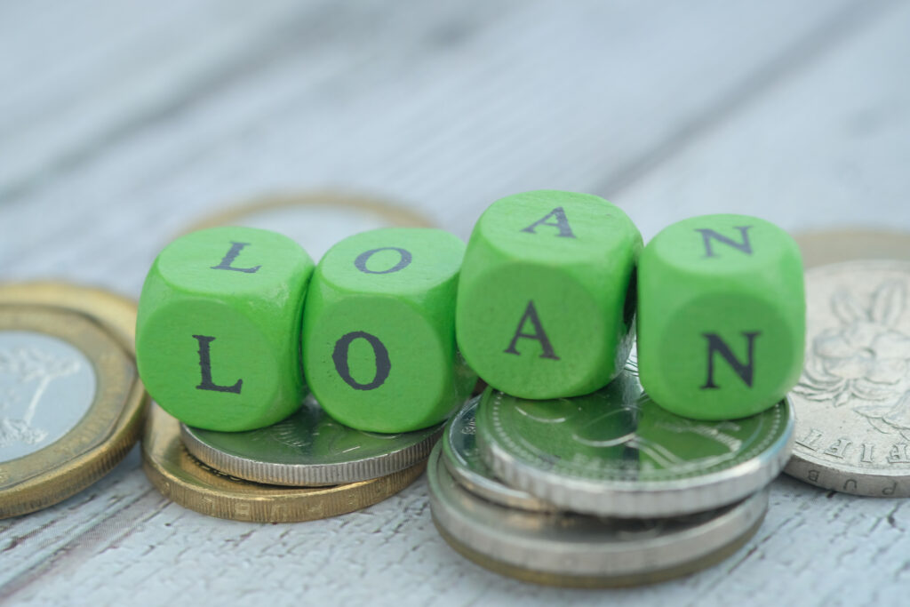 Green blocks forming the word "LOAN" on top of coins. This image could be used to illustrate the idea of obtaining a loan to finance a purchase.