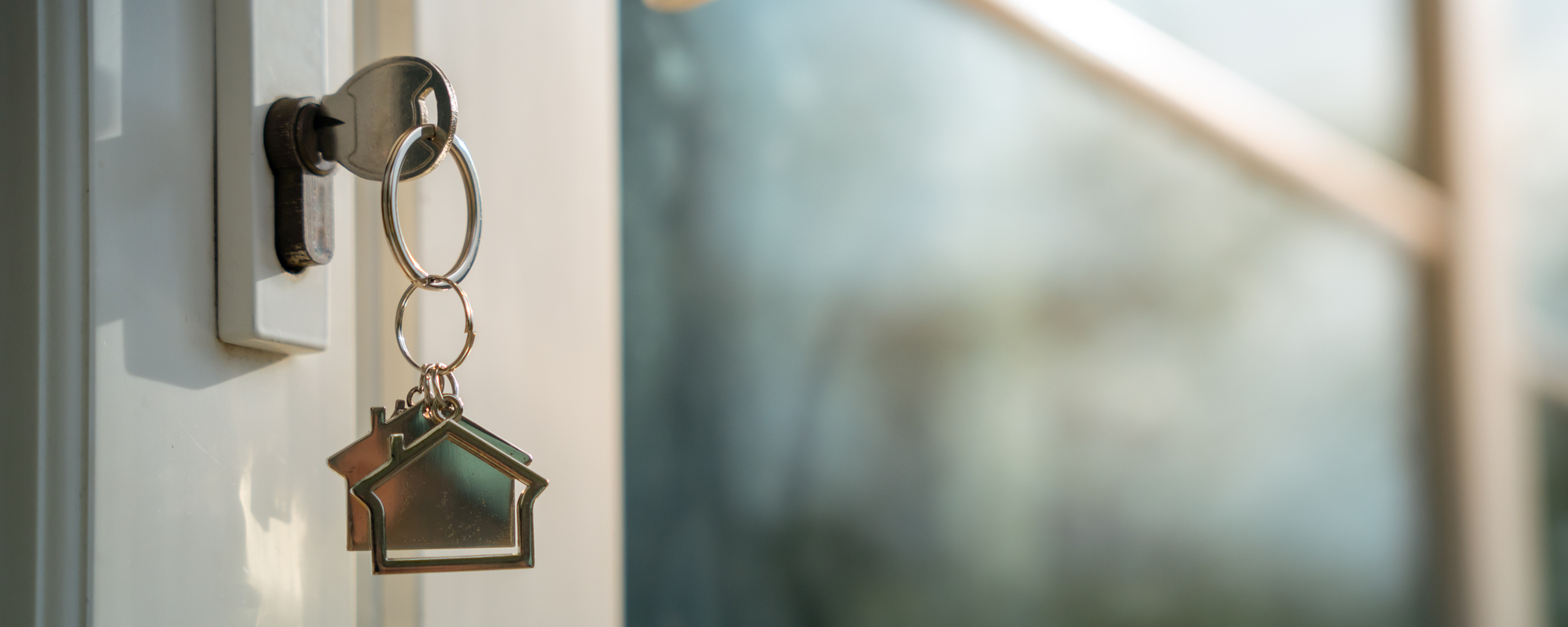 A key with house-shaped charms hanging from it, inserted into a door lock.