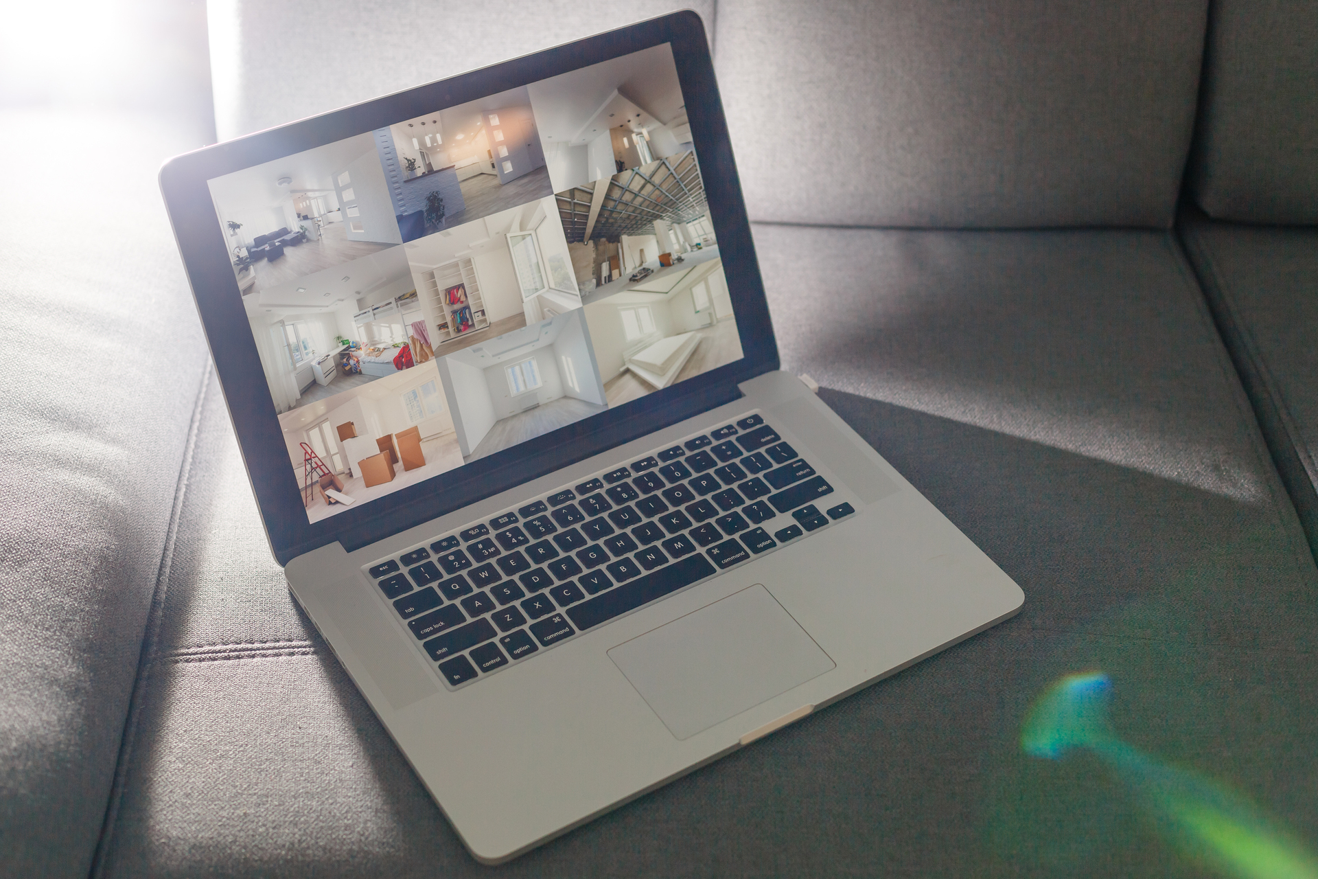 A laptop displaying real estate software on a gray couch, showing multiple property images and detailed listings.