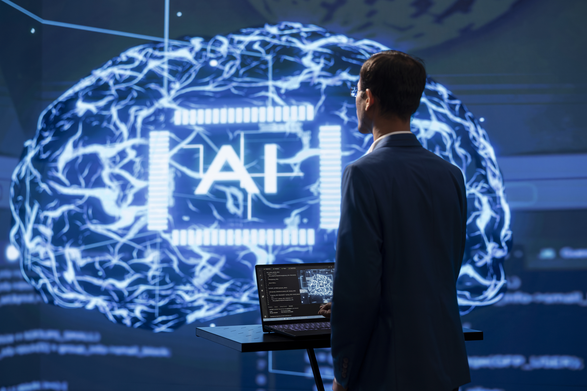 Business professional analyzing AI data visualization on large display showing brain-shaped neural network and 'AI' text, with laptop displaying related code or metrics, suggesting AI feedback and performance analysis in a modern tech environment.